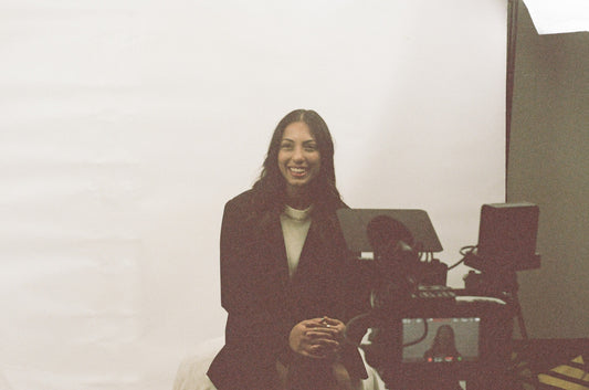 business woman in black blazer and white shirt smiling as hairdresser helps fix her hair in a studio with bright lights and white backdrop set up
