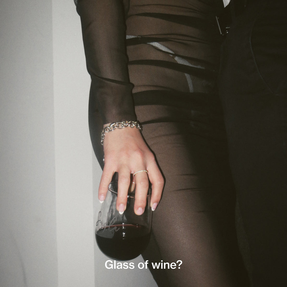 Girl in sheer dress and white underwear holding a glass of red wine with french nails and a silver tiffany bracelet
