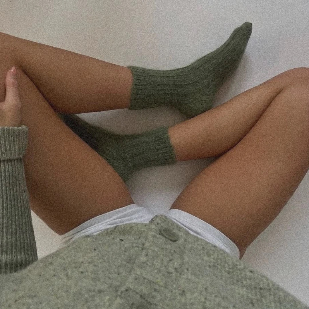 Legs in green wool socks over a soft grey knit